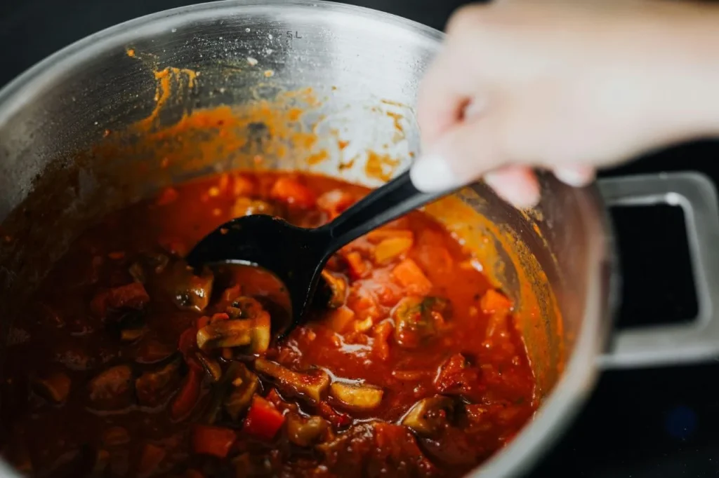 Stirring a large pot of stew with vegetables for batch cooking