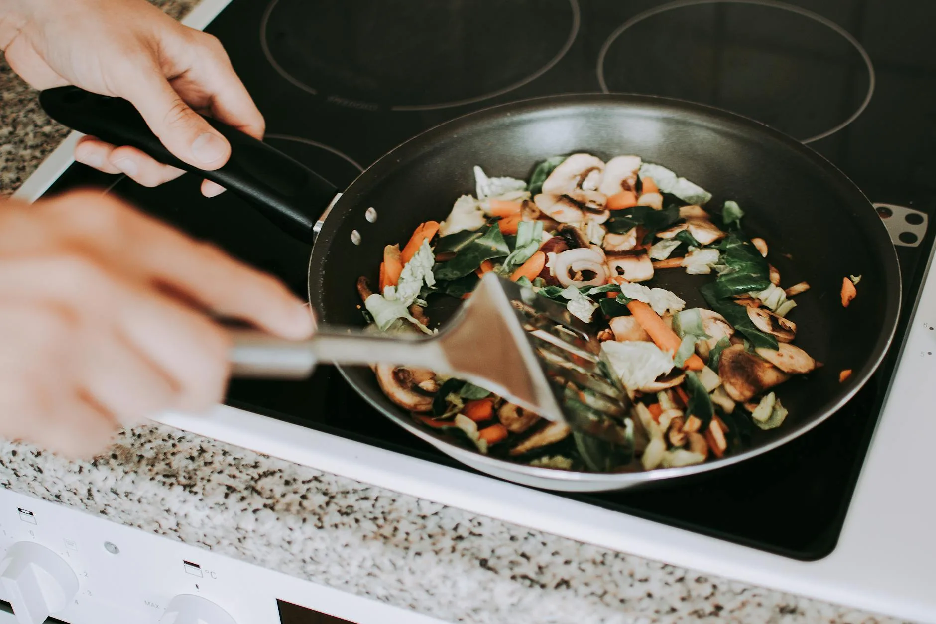 Vegetables being cooked in a frying pan on a kitchen hob