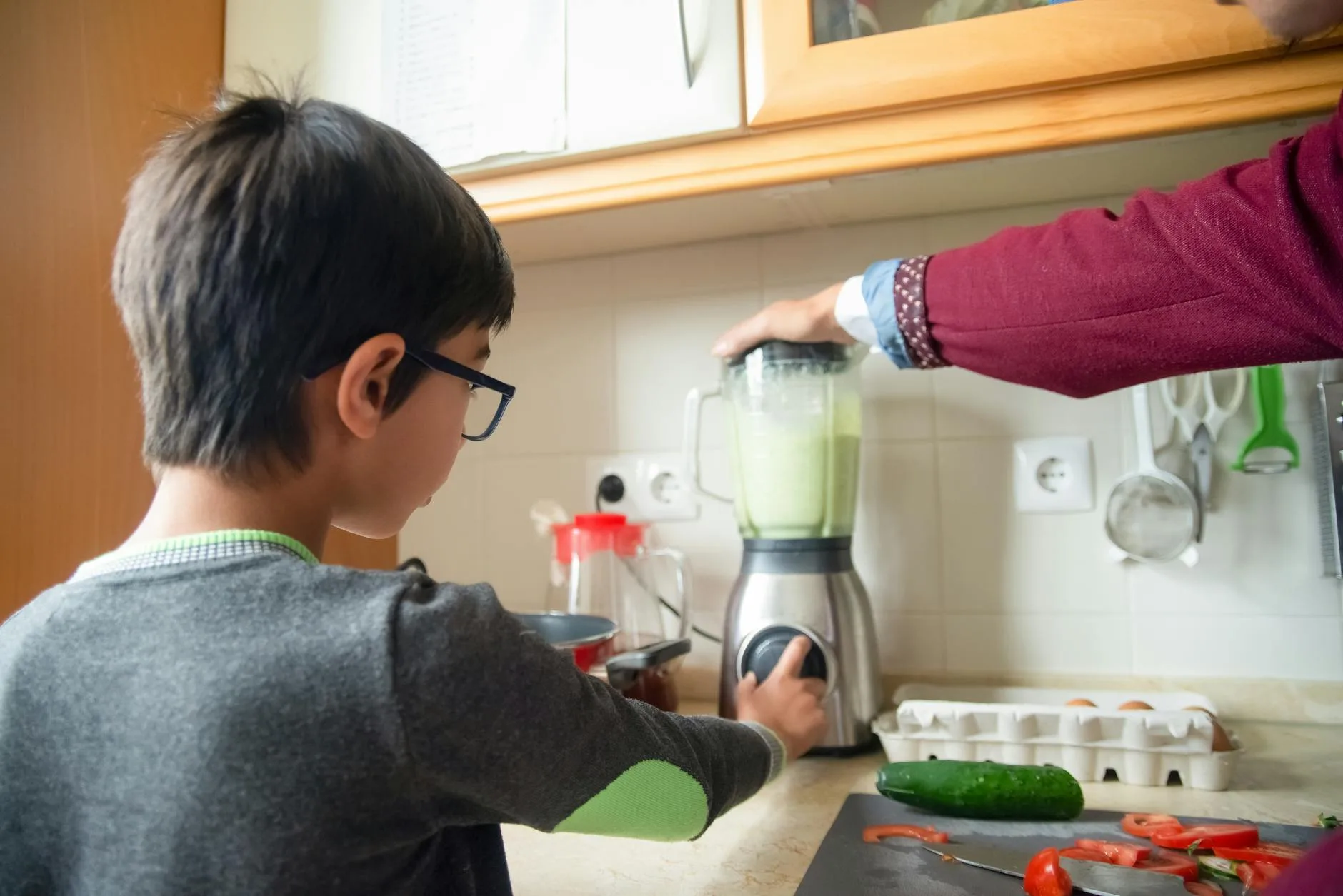 Green smoothie in a glass next to a blender in a kitchen