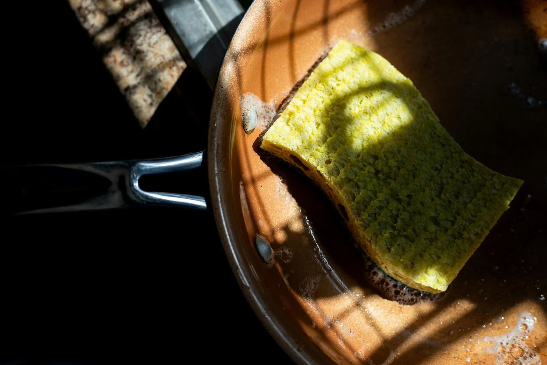 Hand washing a baking tray with soapy sponge in a sink