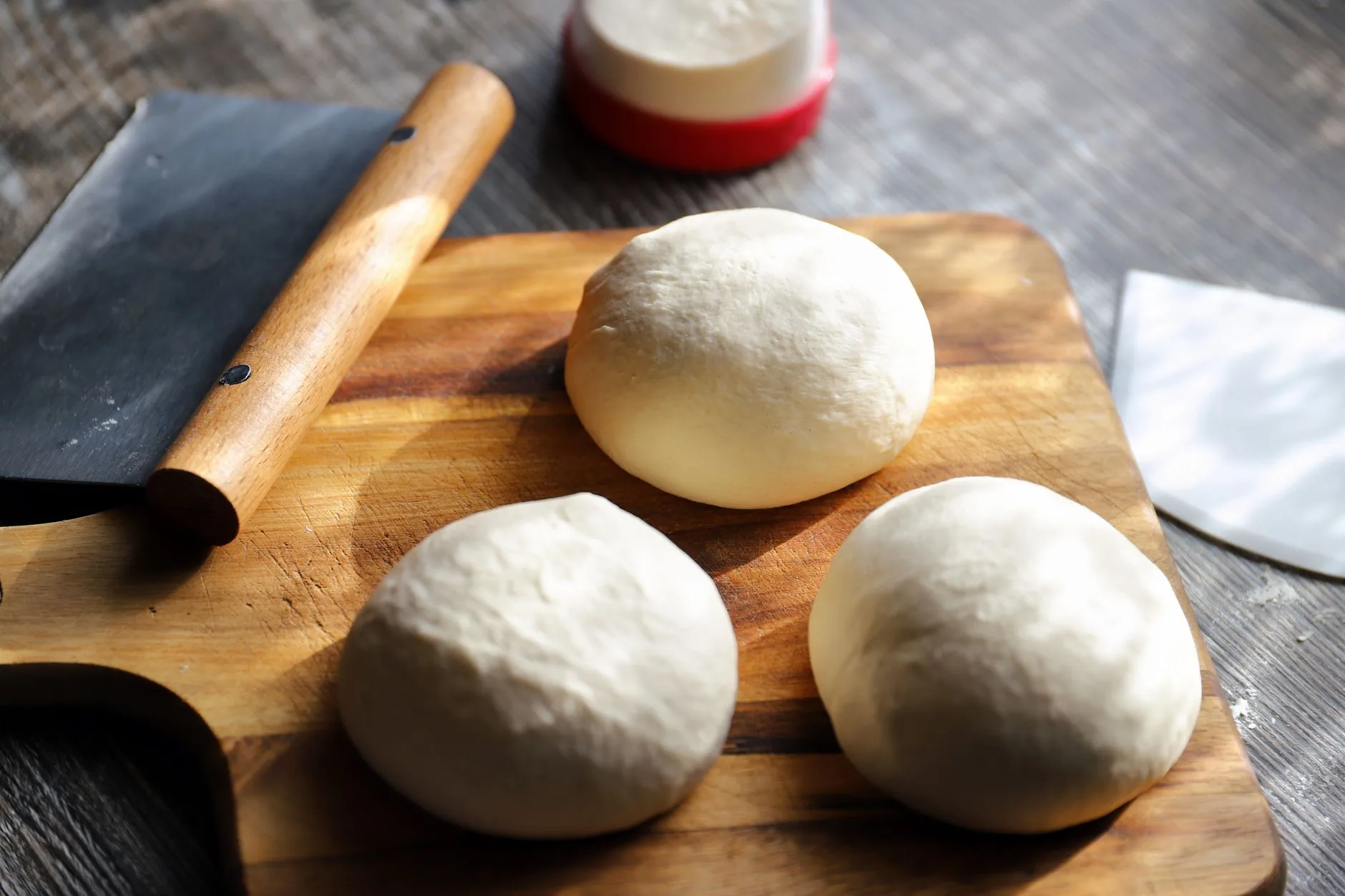 Pizza dough balls on a board beside baking tools